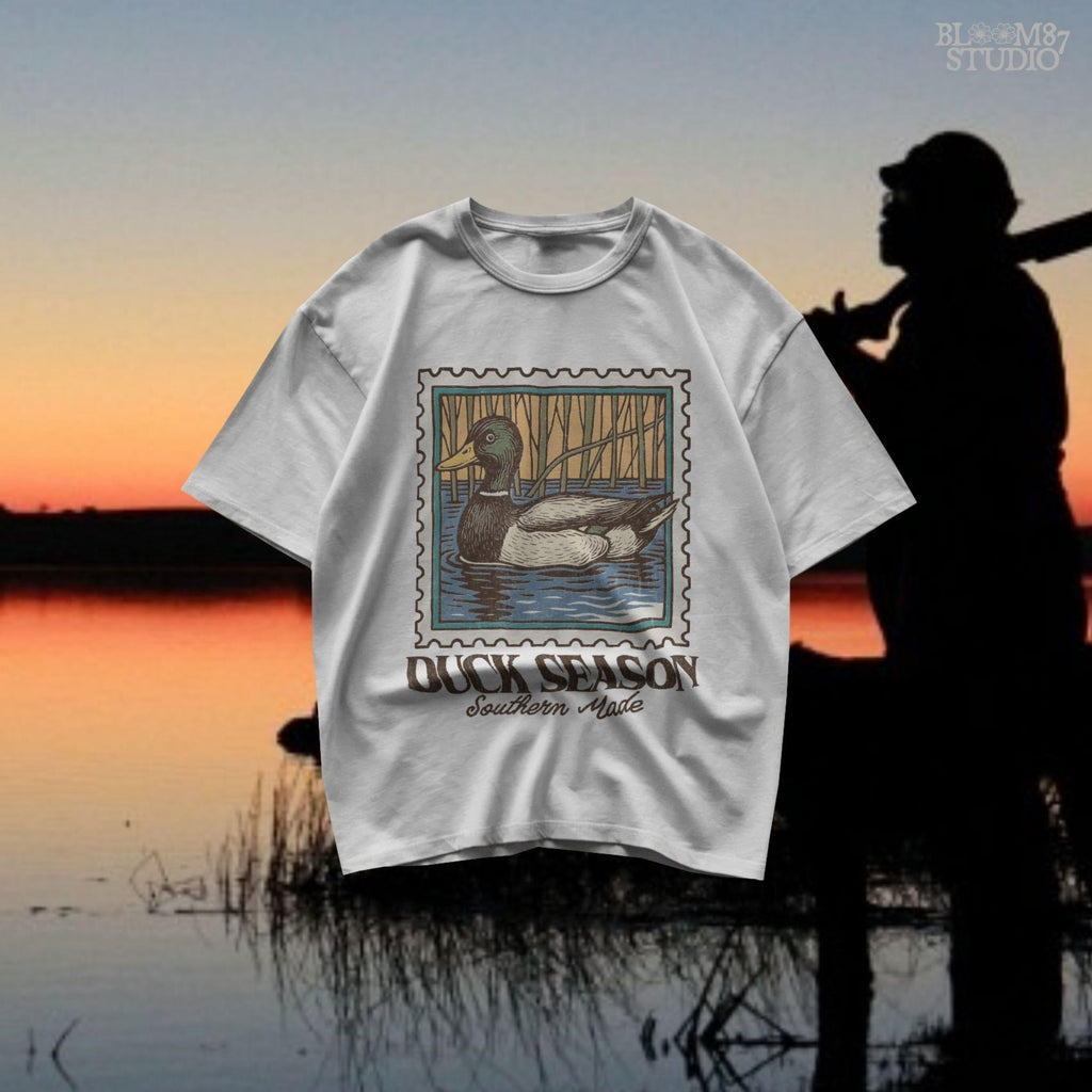Vintage stamp-style mallard duck floating in water with forest background and text “Duck Season – Southern Made” in retro serif font.