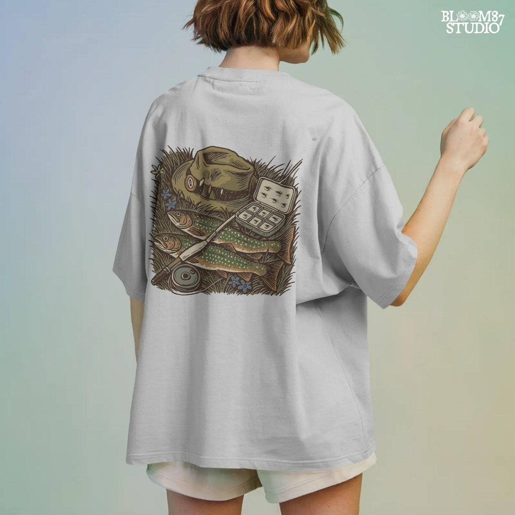 Vintage fly fishing illustration showing two trout, a fly rod, fisherman’s hat, and fly box on grassy ground with wildflowers.