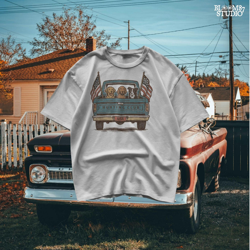 Three hunting dogs in the back of a blue vintage pickup truck with USA flags and “Hunting Club” text, patriotic hunting design for dog lovers.