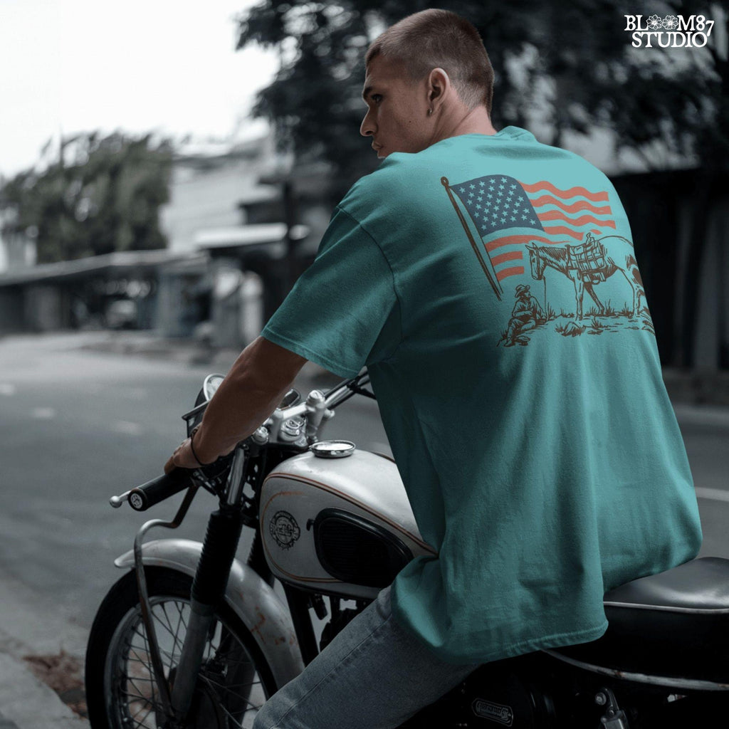 Vintage-style illustration of a cowboy sitting beside a saddled horse under a waving American flag.