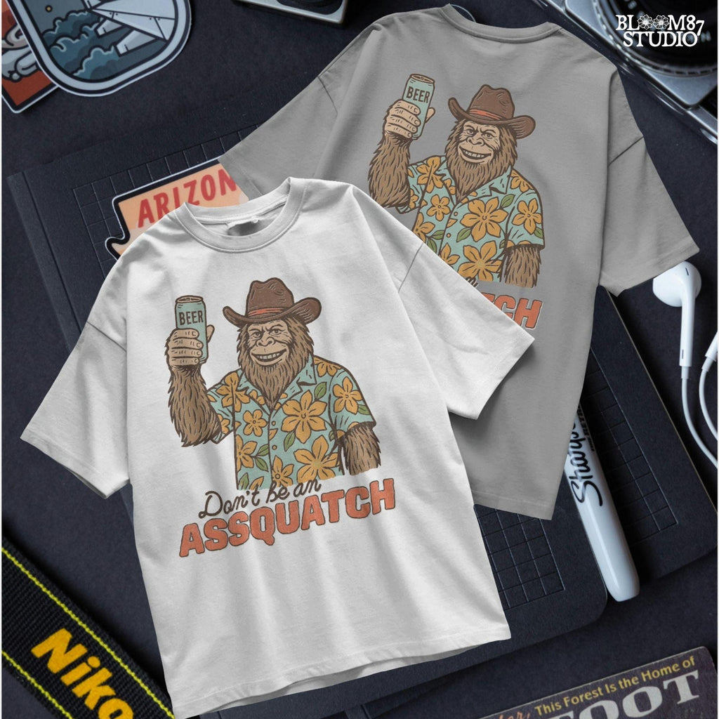Retro cartoon Sasquatch in floral shirt holding a beer can with text “Don’t Be an Assquatch,” perfect for funny camping or summer designs