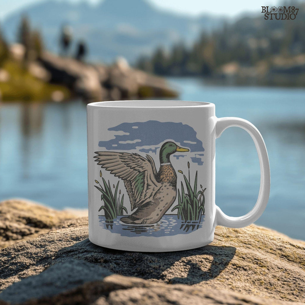 Vintage illustration of a mallard duck with wings spread standing in a pond with reeds and a cloudy blue sky – rustic nature sublimation PNG.