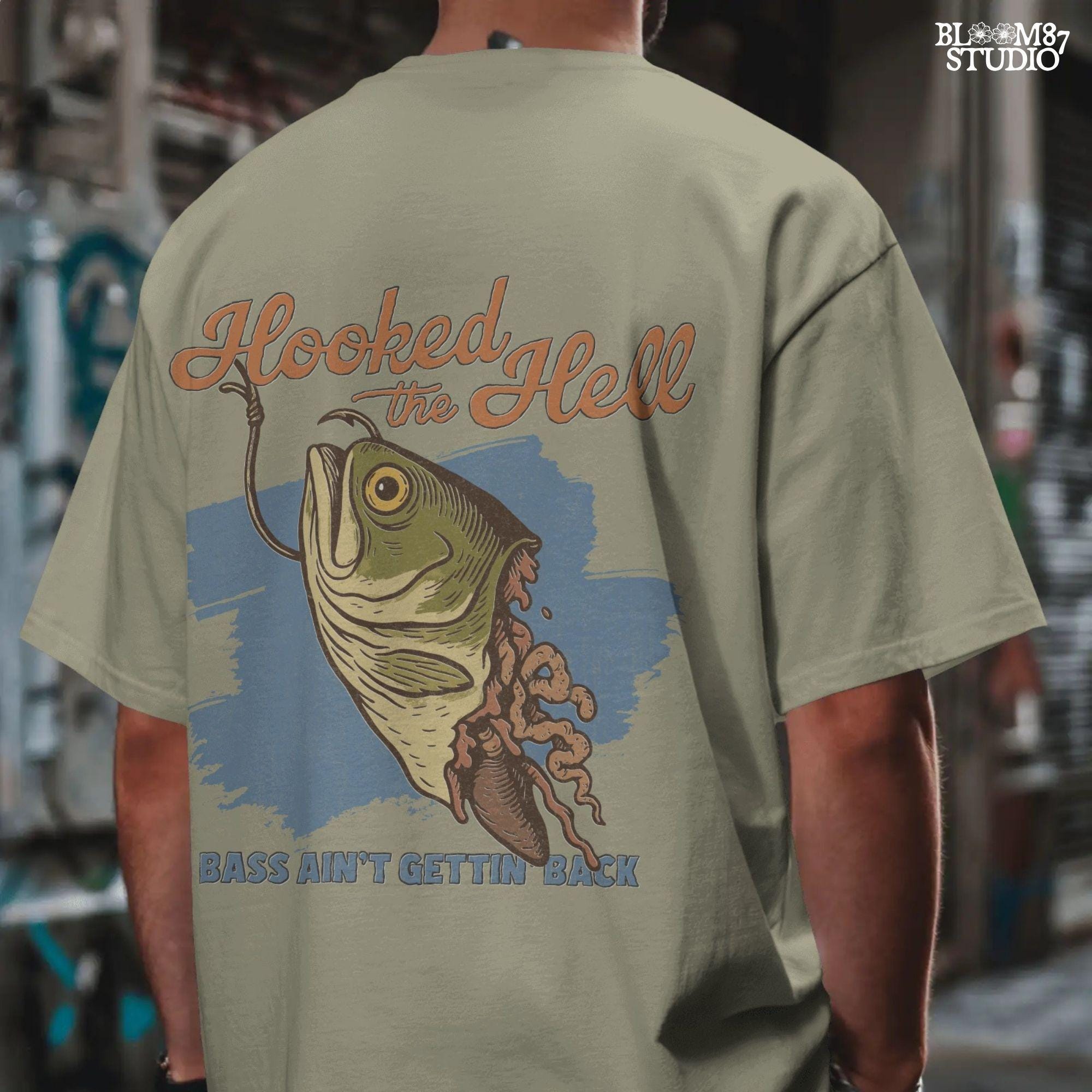 Funny exaggerated bass fish graphic with a hook through its mouth and dramatic detailing, paired with the text “Hooked the Hell” and “Bass Ain’t Gettin Back.”