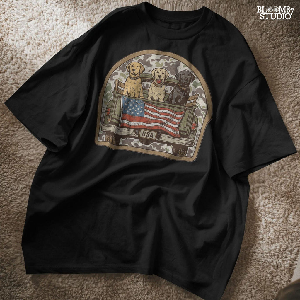 Three Labrador retrievers — yellow, chocolate, and black — sitting on the back of a green camouflage pickup truck with an American flag and the words “Local Boy” underneath.