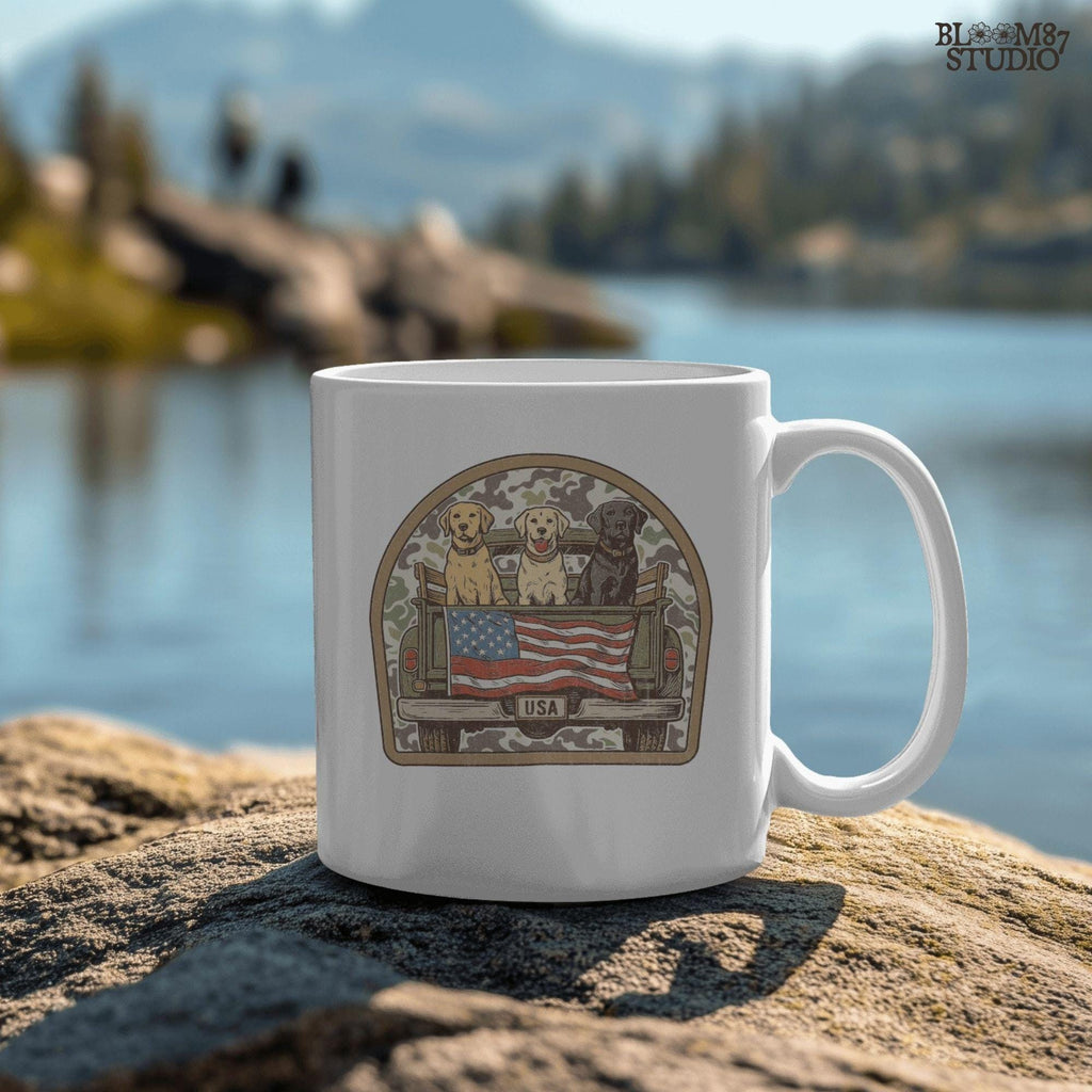 Three Labrador retrievers — yellow, chocolate, and black — sitting on the back of a green camouflage pickup truck with an American flag and the words “Local Boy” underneath.