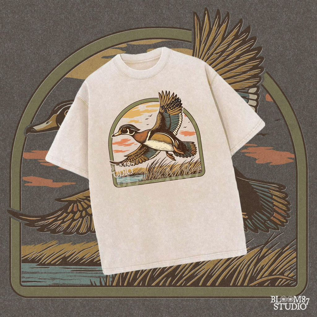 Illustration of a wood duck flying above a marsh at sunset with warm-toned clouds, cattails, and a reflective waterline.