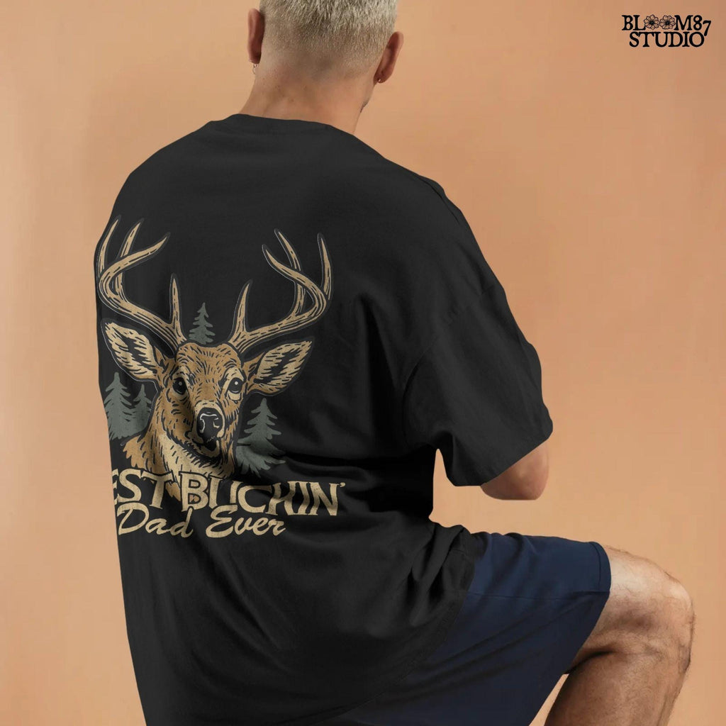 Rustic illustration of a buck deer with antlers and pine trees, text below says “Best Buckin’ Dad Ever” in bold and script font