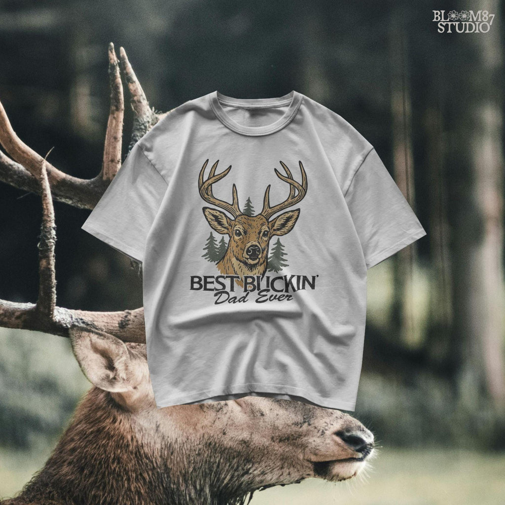 Rustic illustration of a buck deer with antlers and pine trees, text below says “Best Buckin’ Dad Ever” in bold and script font
