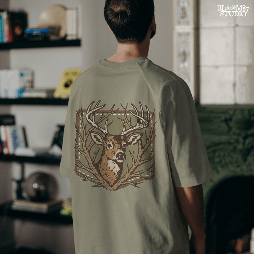 Stylized deer head with antlers framed by bare branches, placed on an olive green patch background with stitching detail.