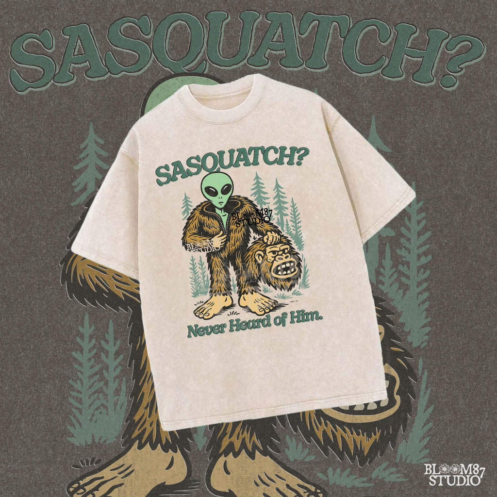 Funny alien unzipping a Bigfoot costume with Sasquatch head in hand, forest trees in background, and text “Sasquatch? Never Heard of Him.”