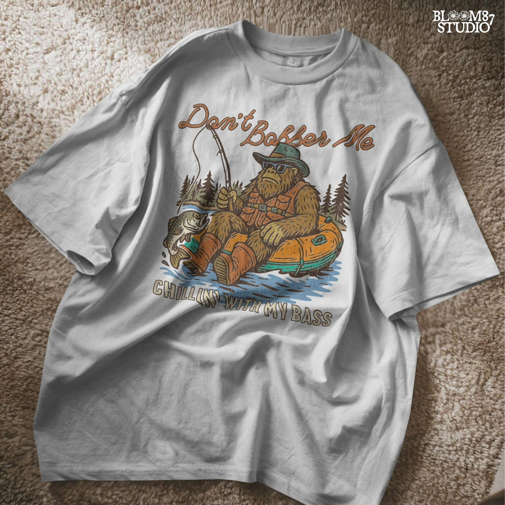 Funny Bigfoot sitting in a float tube holding a fishing rod and bass fish, wearing sunglasses and vest, with text “Don’t Bobber Me – Chillin’ with My Bass.”