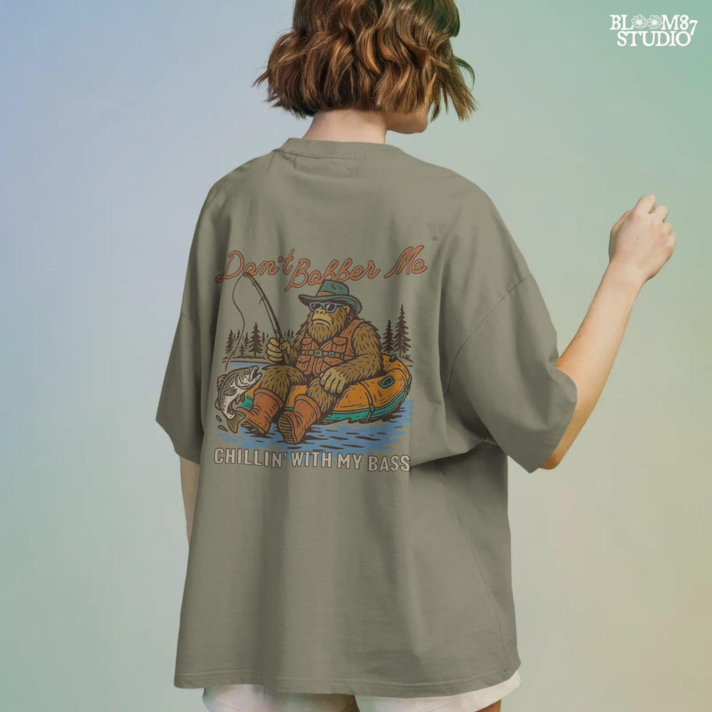 Funny Bigfoot sitting in a float tube holding a fishing rod and bass fish, wearing sunglasses and vest, with text “Don’t Bobber Me – Chillin’ with My Bass.”