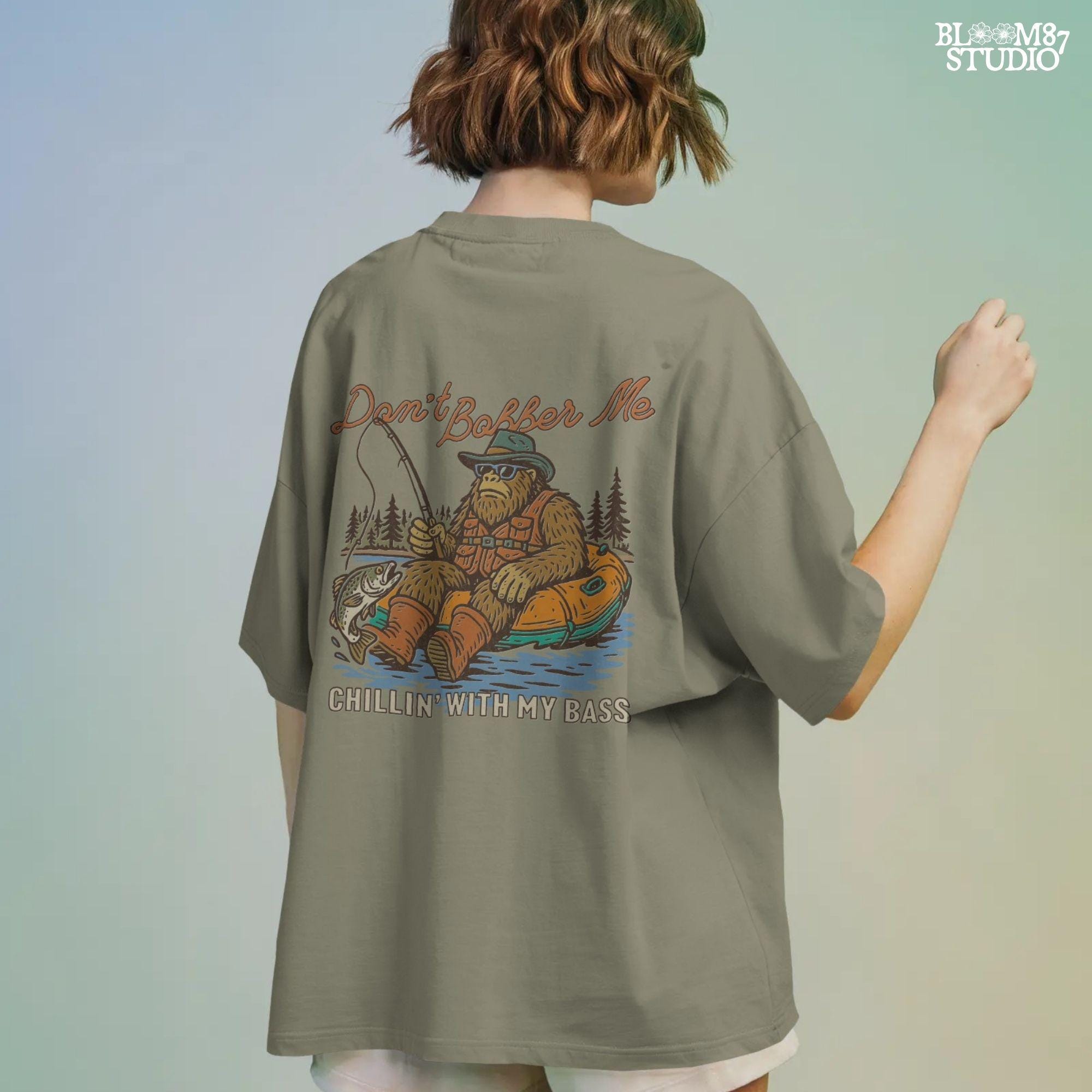 Funny Bigfoot sitting in a float tube holding a fishing rod and bass fish, wearing sunglasses and vest, with text “Don’t Bobber Me – Chillin’ with My Bass.”