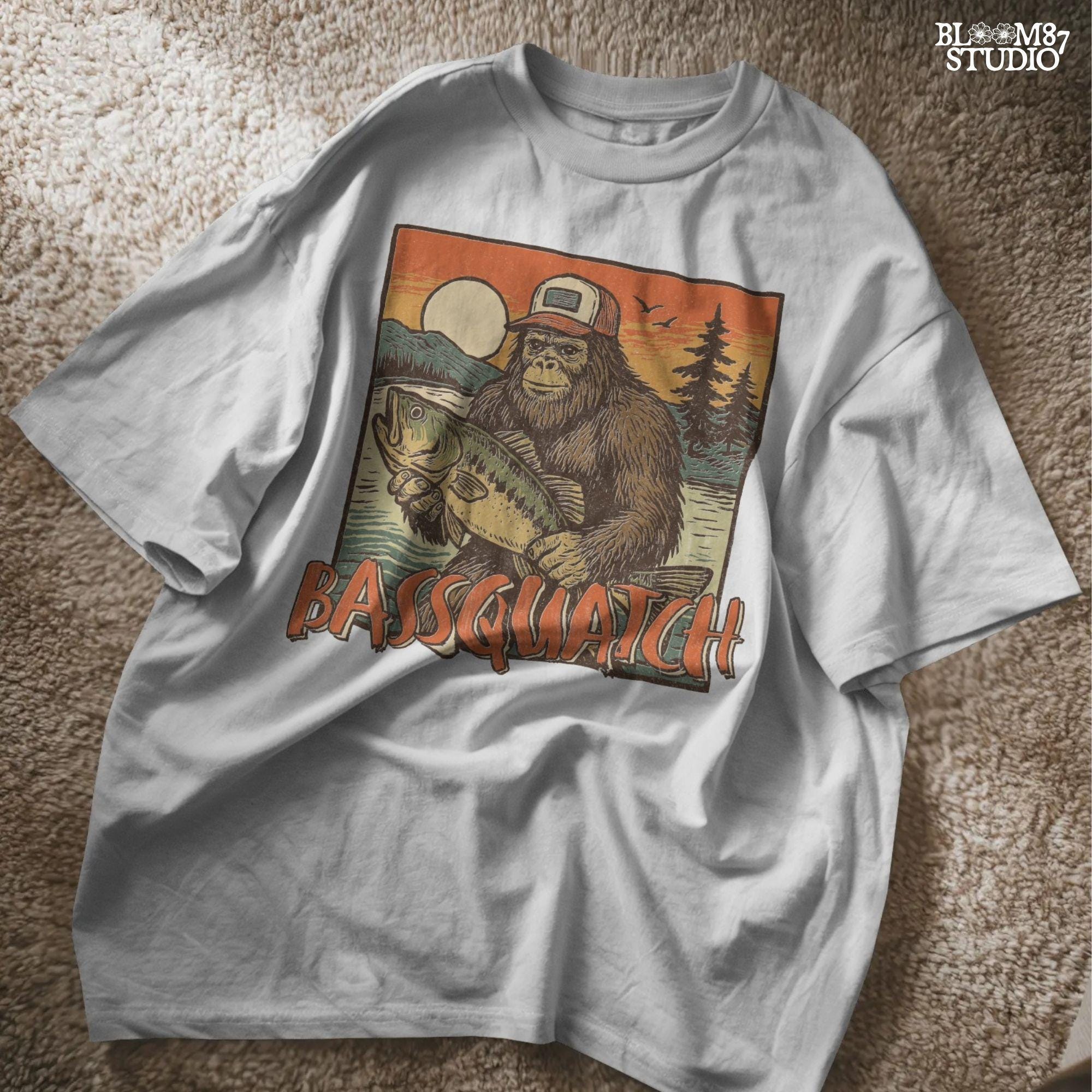 Bigfoot holding a large bass at sunset with summer lake background and the word “Bassquatch” in bold orange letters.