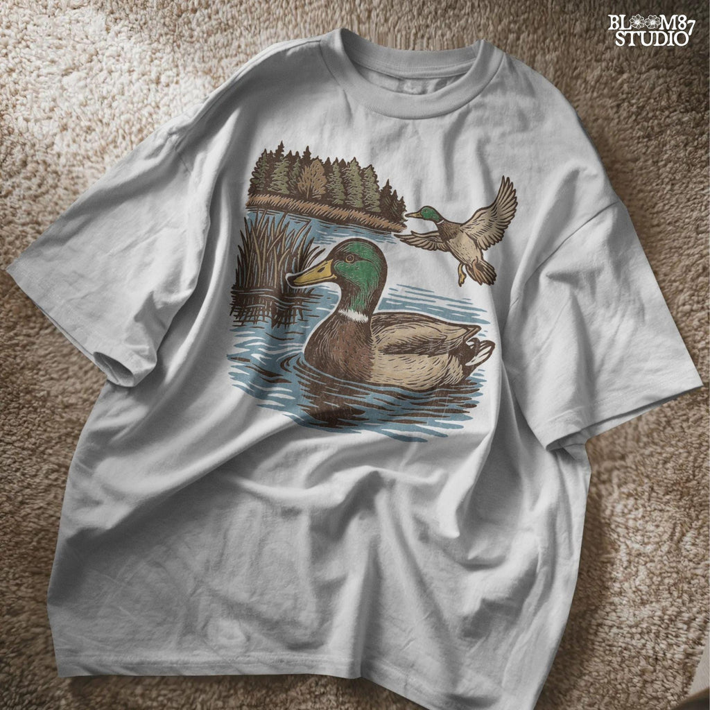 Two mallard ducks in a peaceful summer lake scene with pine trees and blue water, one swimming and one flying.