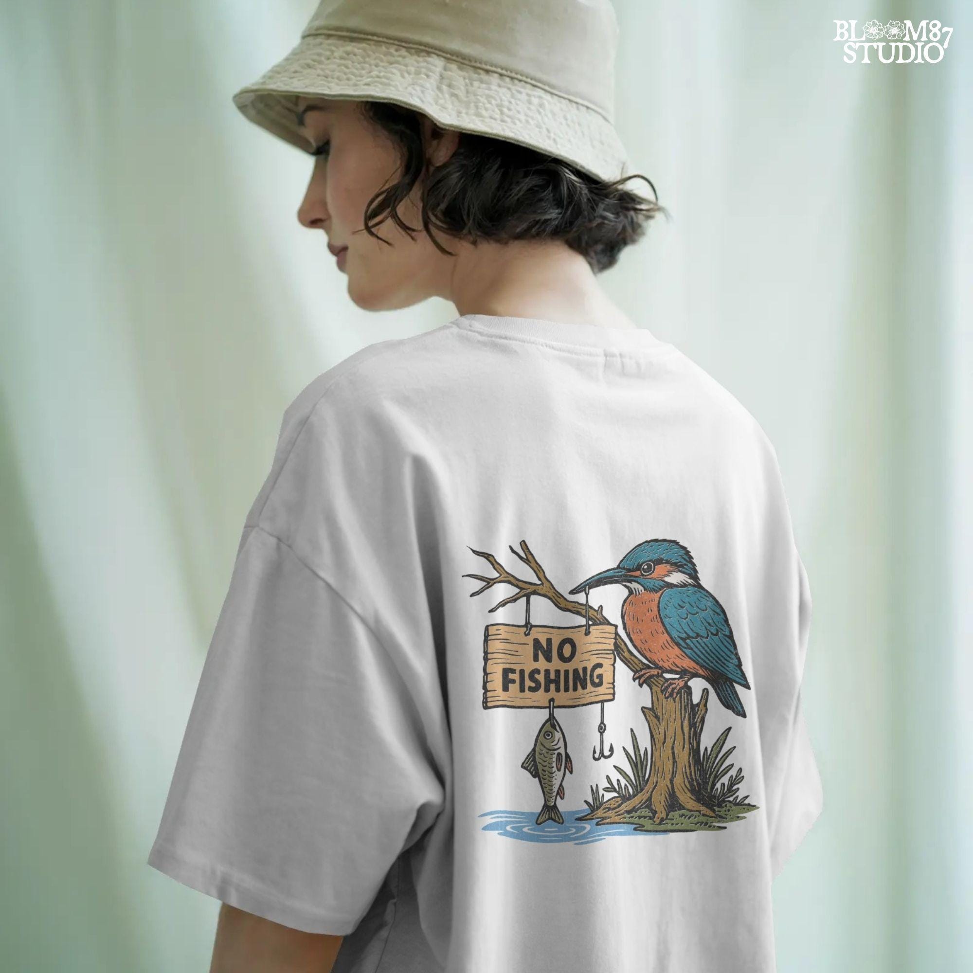 Cartoon kingfisher bird sitting on a tree holding a “No Fishing” sign with a fish hanging below, in a humorous lake life design