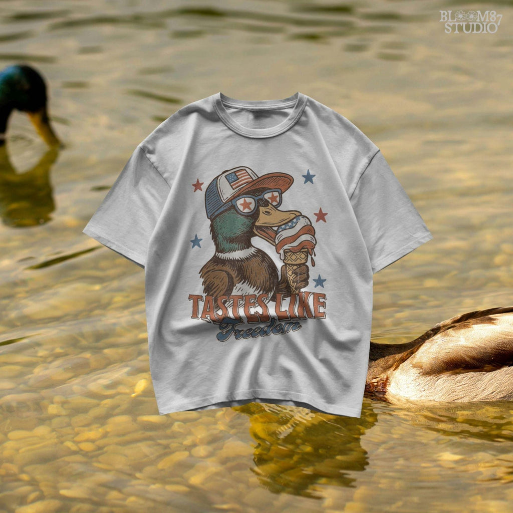Funny cartoon duck wearing USA hat and star sunglasses, licking patriotic ice cream cone with “Tastes Like Freedom” text and red-white-blue stars