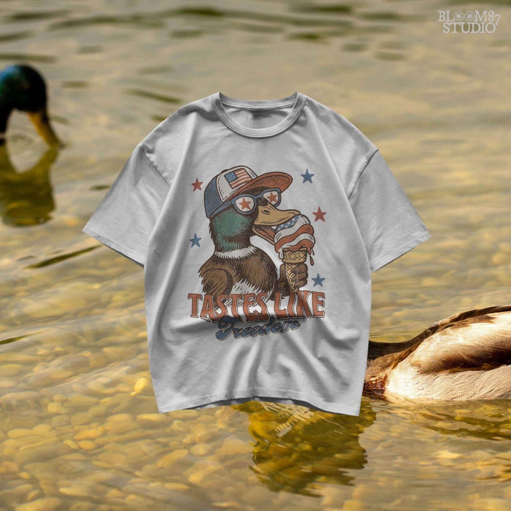 Funny cartoon duck wearing USA hat and star sunglasses, licking patriotic ice cream cone with “Tastes Like Freedom” text and red-white-blue stars