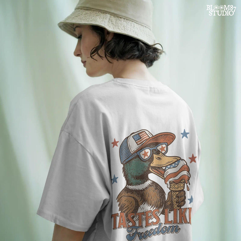Funny cartoon duck wearing USA hat and star sunglasses, licking patriotic ice cream cone with “Tastes Like Freedom” text and red-white-blue stars
