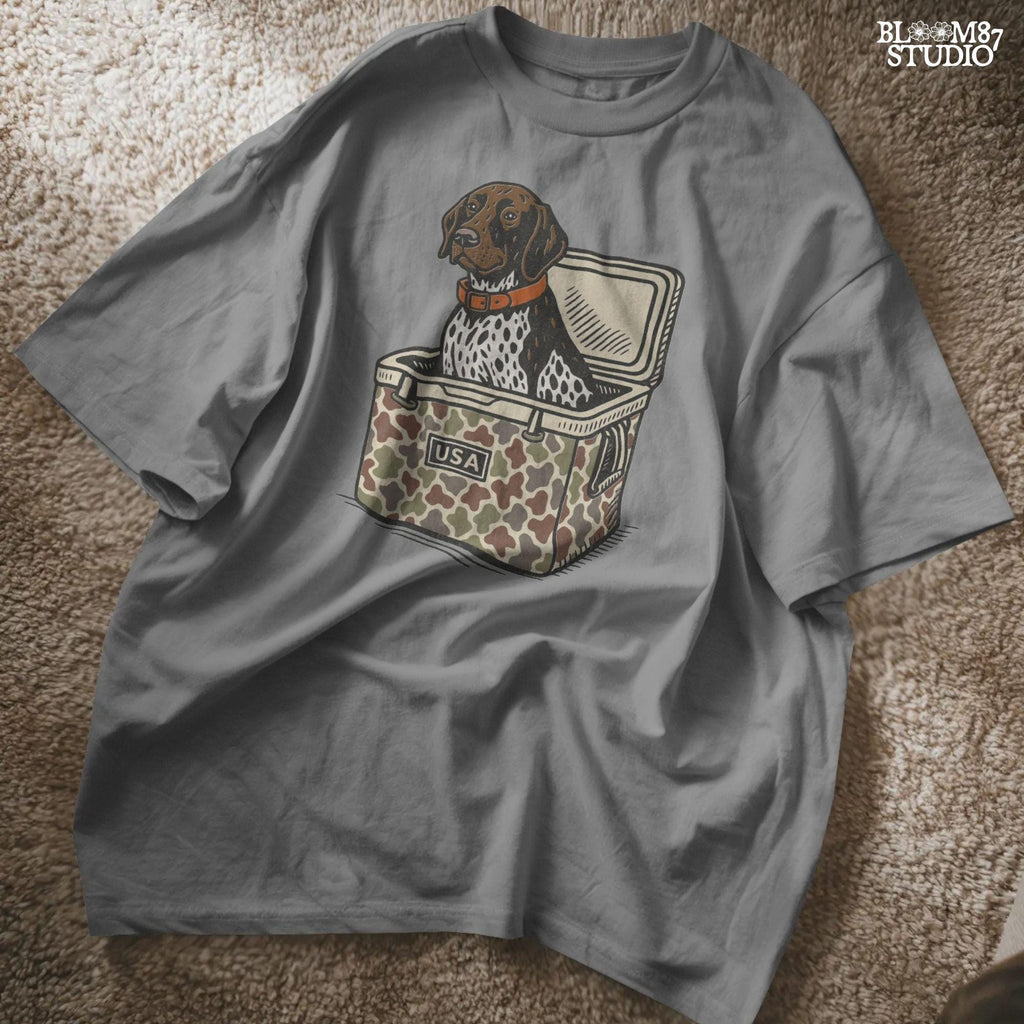 German Shorthaired Pointer dog sitting inside camouflage cooler labeled “USA,” in rustic cartoon patriotic style