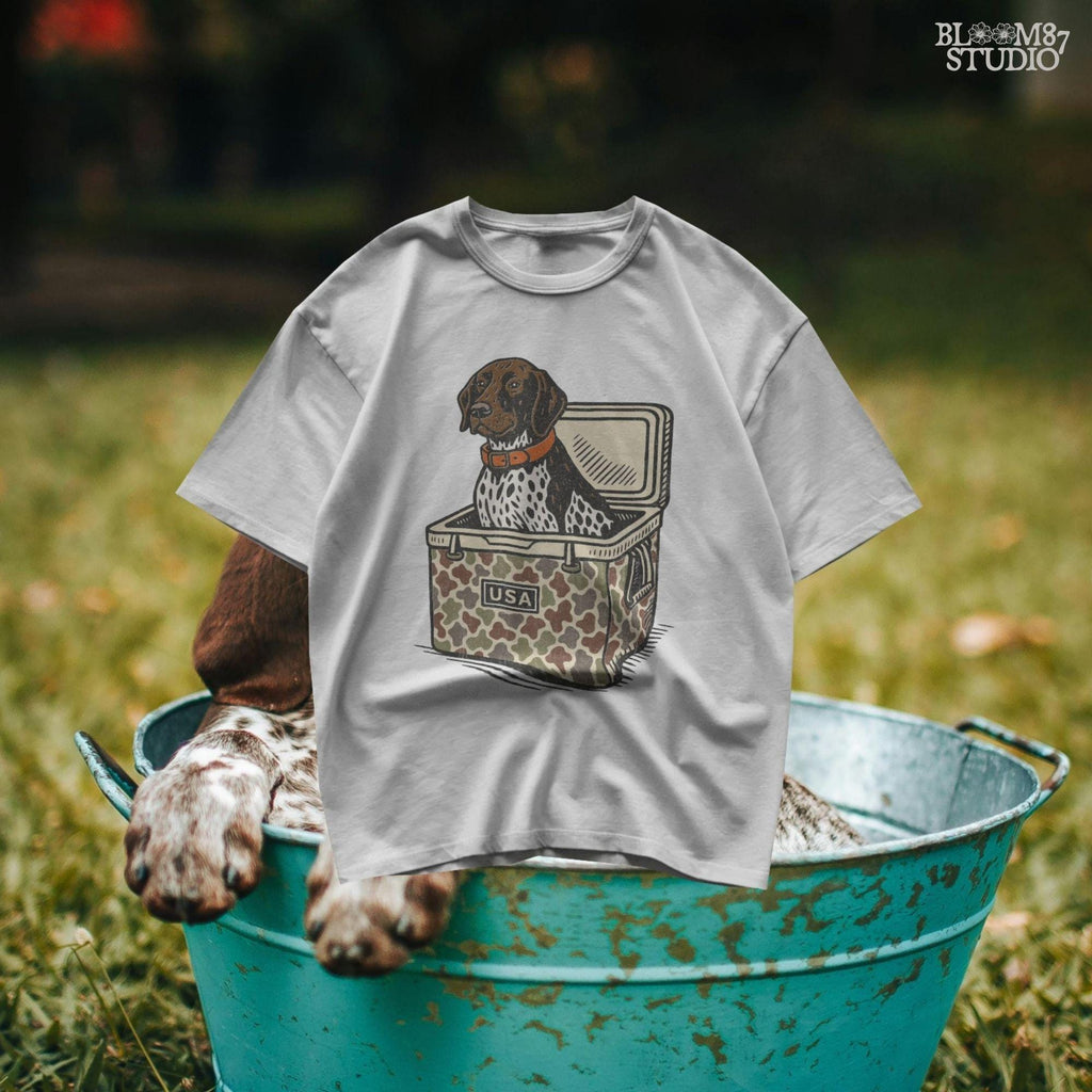 German Shorthaired Pointer dog sitting inside camouflage cooler labeled “USA,” in rustic cartoon patriotic style