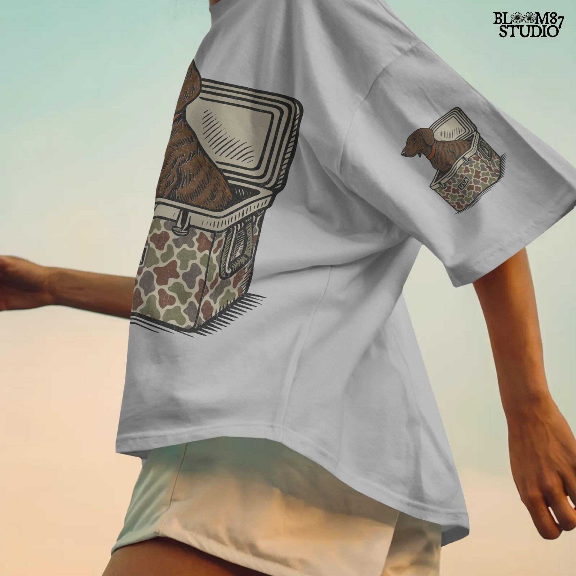 Brown dachshund dog sitting in camouflage cooler labeled “USA” with a red collar, drawn in patriotic cartoon style