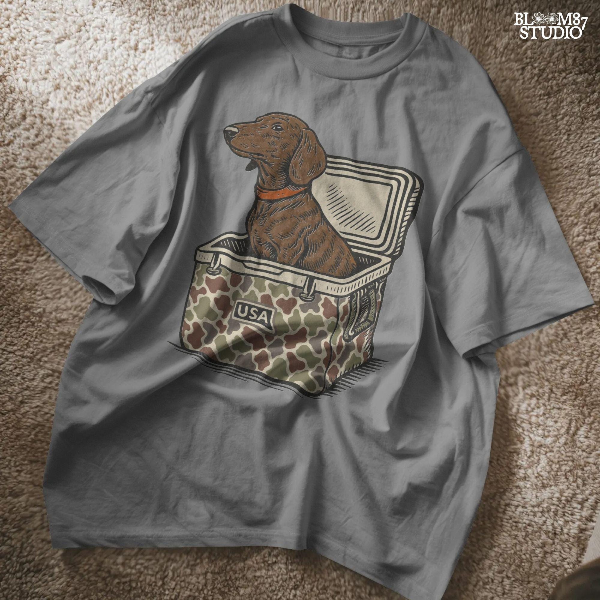 Brown dachshund dog sitting in camouflage cooler labeled “USA” with a red collar, drawn in patriotic cartoon style