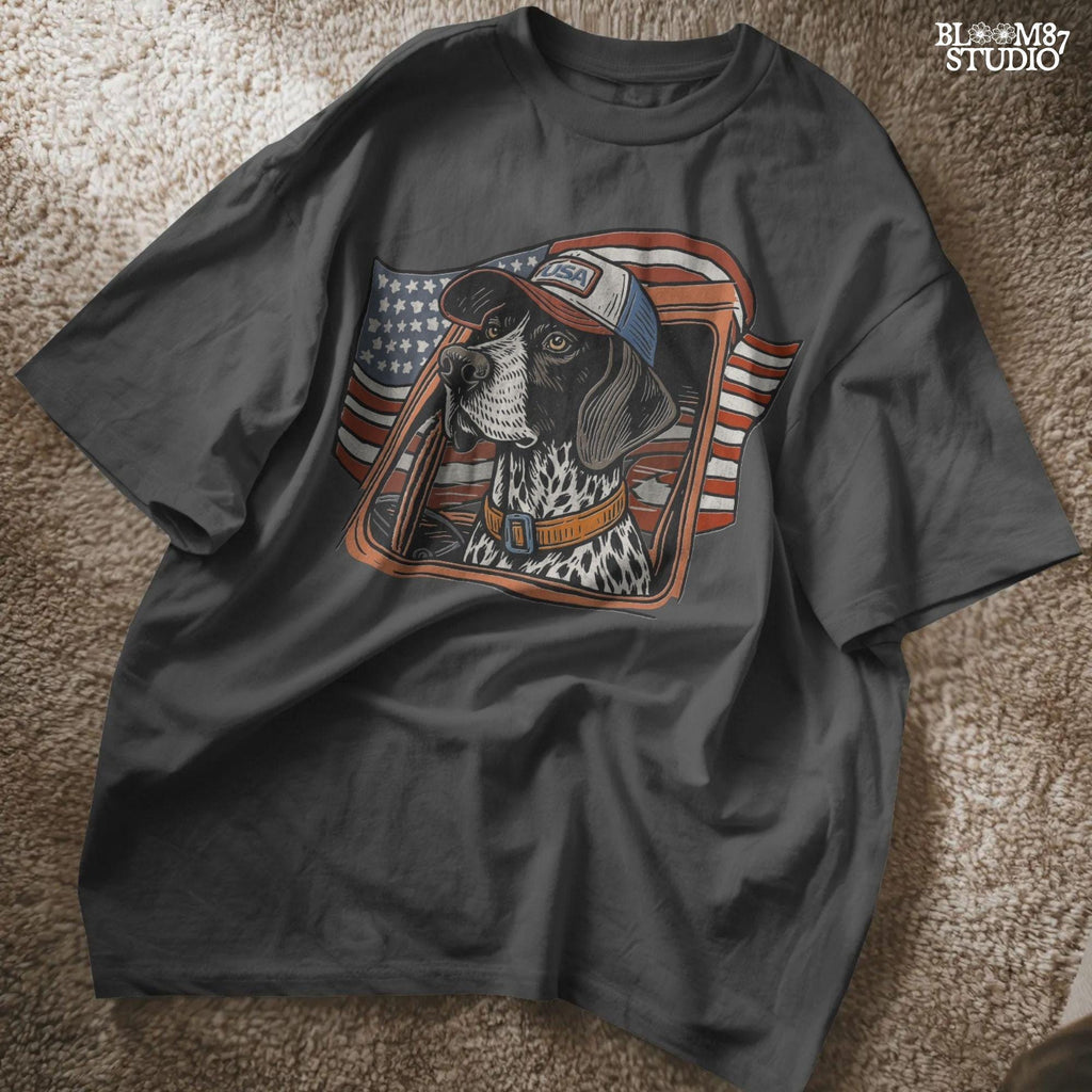 German Shorthaired Pointer dog wearing USA hat looking out of truck window with American flag waving in background