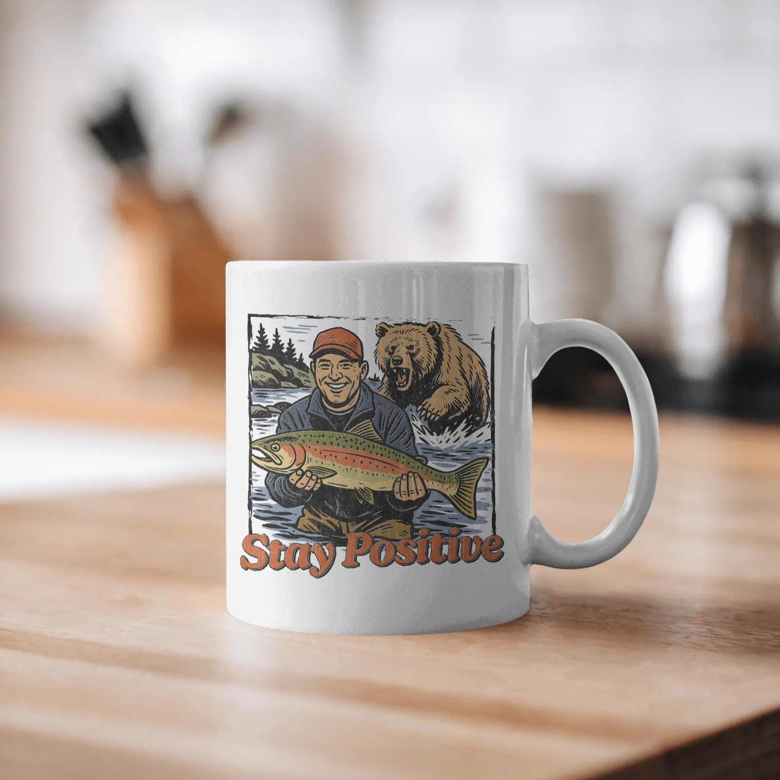 Happy fisherman holding large trout in river while a grizzly bear charges from behind, with text “Stay Positive” in funny outdoor design style
