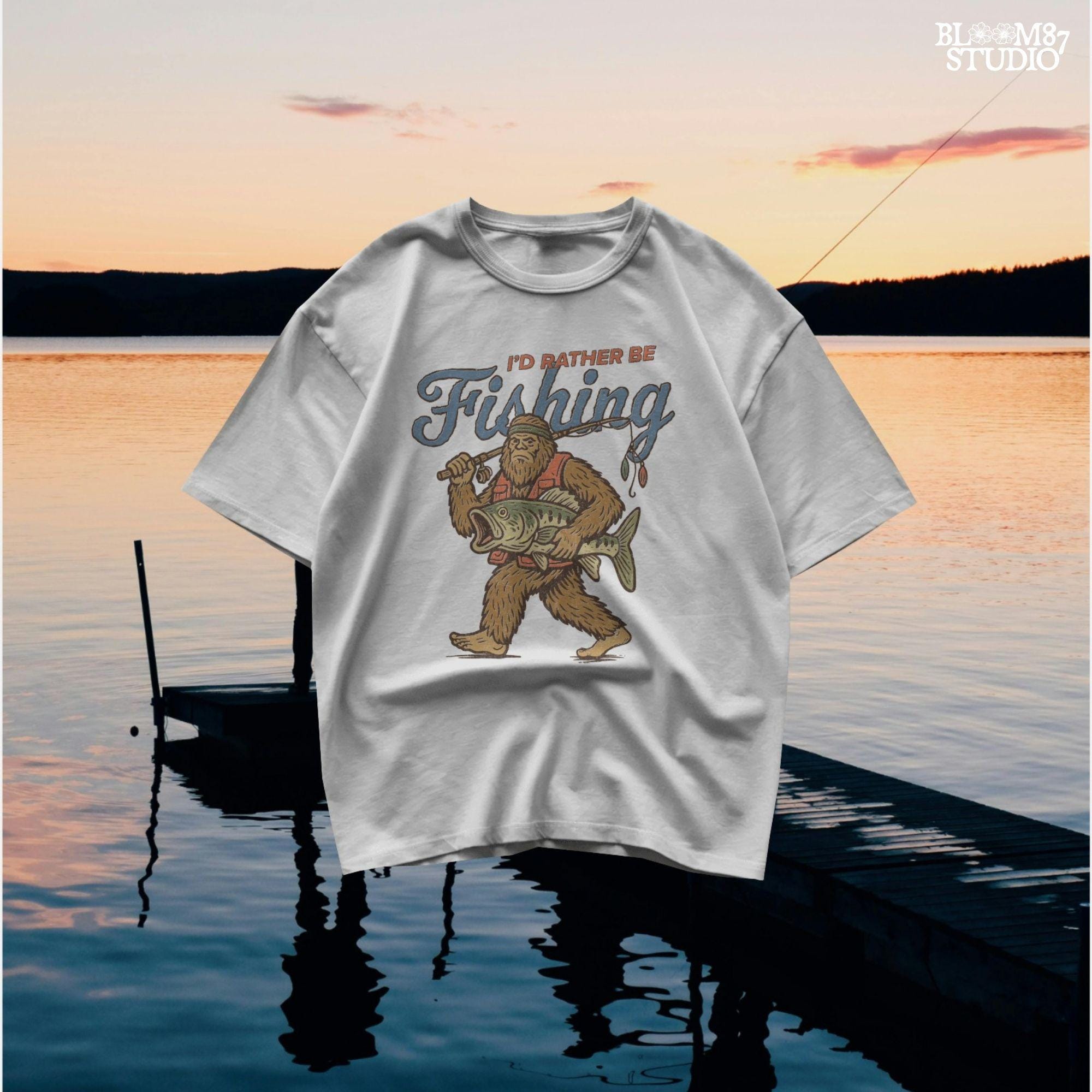 Funny vintage illustration of Bigfoot wearing a fishing vest, holding a giant bass and fishing rod, with text that reads “I’d Rather Be Fishing.”