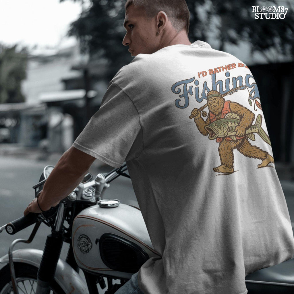 Funny vintage illustration of Bigfoot wearing a fishing vest, holding a giant bass and fishing rod, with text that reads “I’d Rather Be Fishing.”