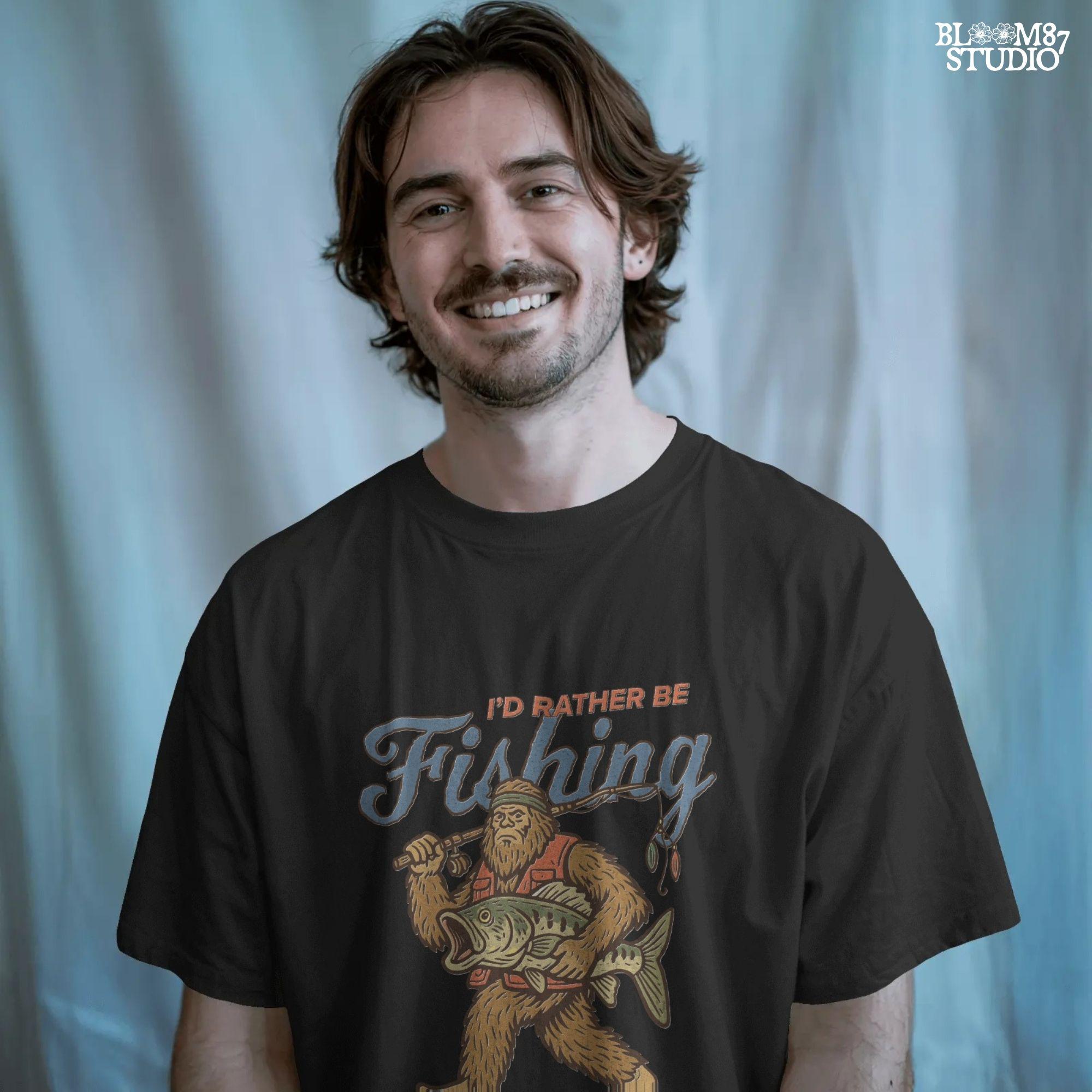 Funny vintage illustration of Bigfoot wearing a fishing vest, holding a giant bass and fishing rod, with text that reads “I’d Rather Be Fishing.”