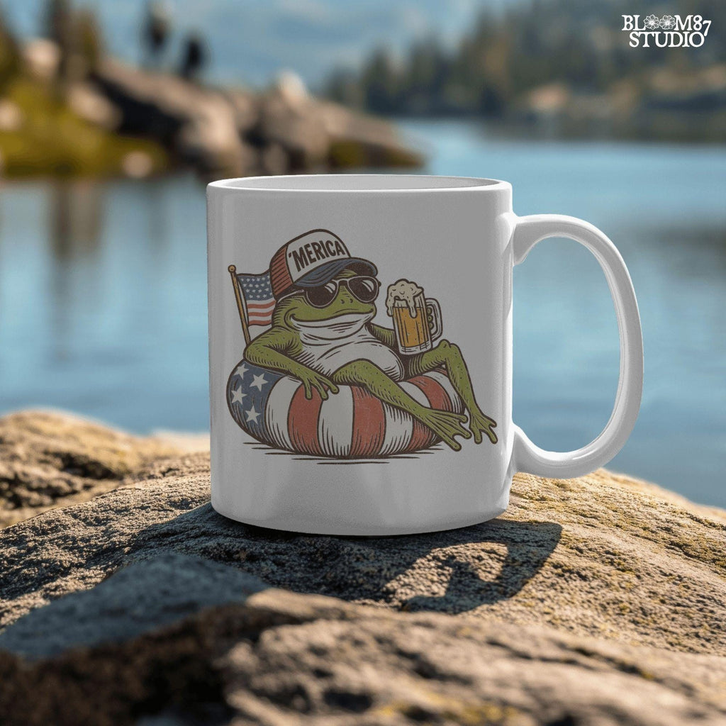 A vintage-style cartoon frog lounging on a patriotic inner tube, wearing a ‘Merica cap and sunglasses, holding a mug of beer with an American flag in the background.