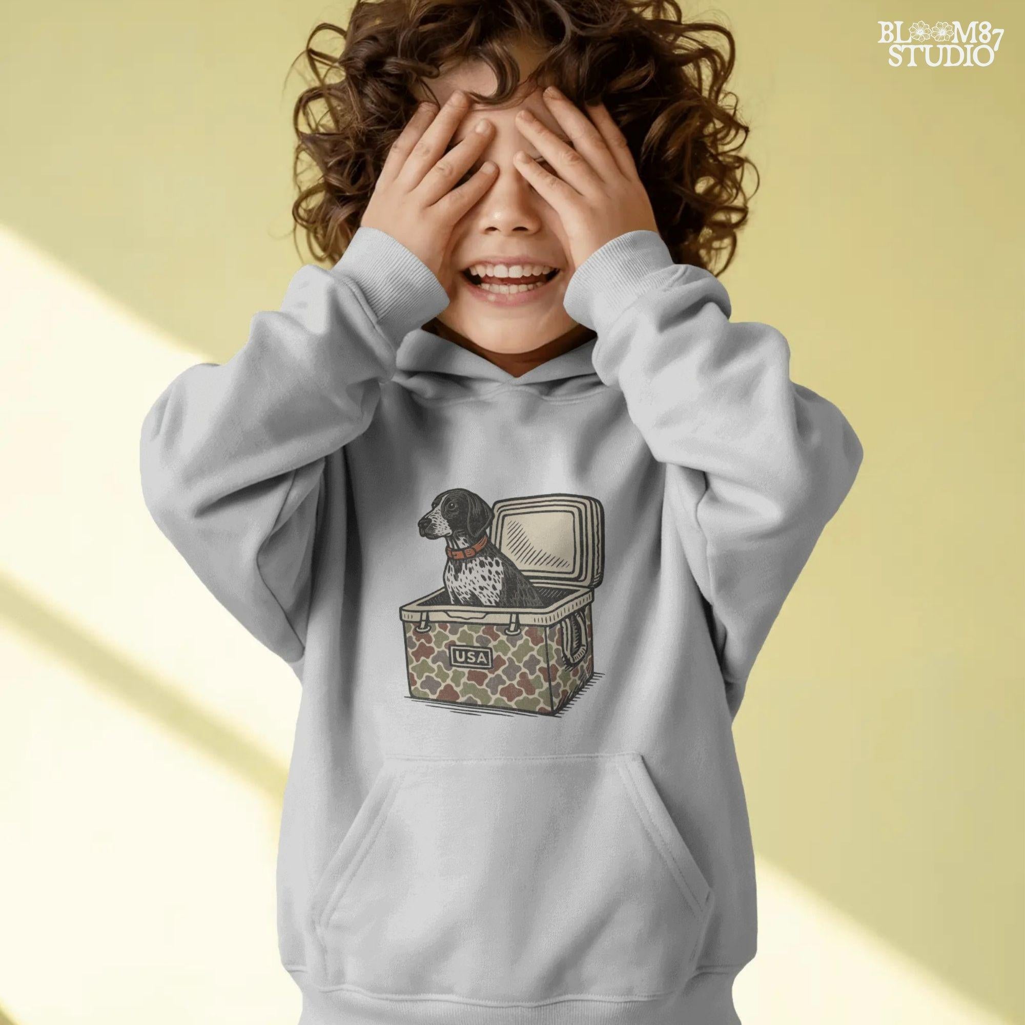 German Shorthaired Pointer dog sitting inside camouflage cooler labeled “USA,” in rustic cartoon patriotic style