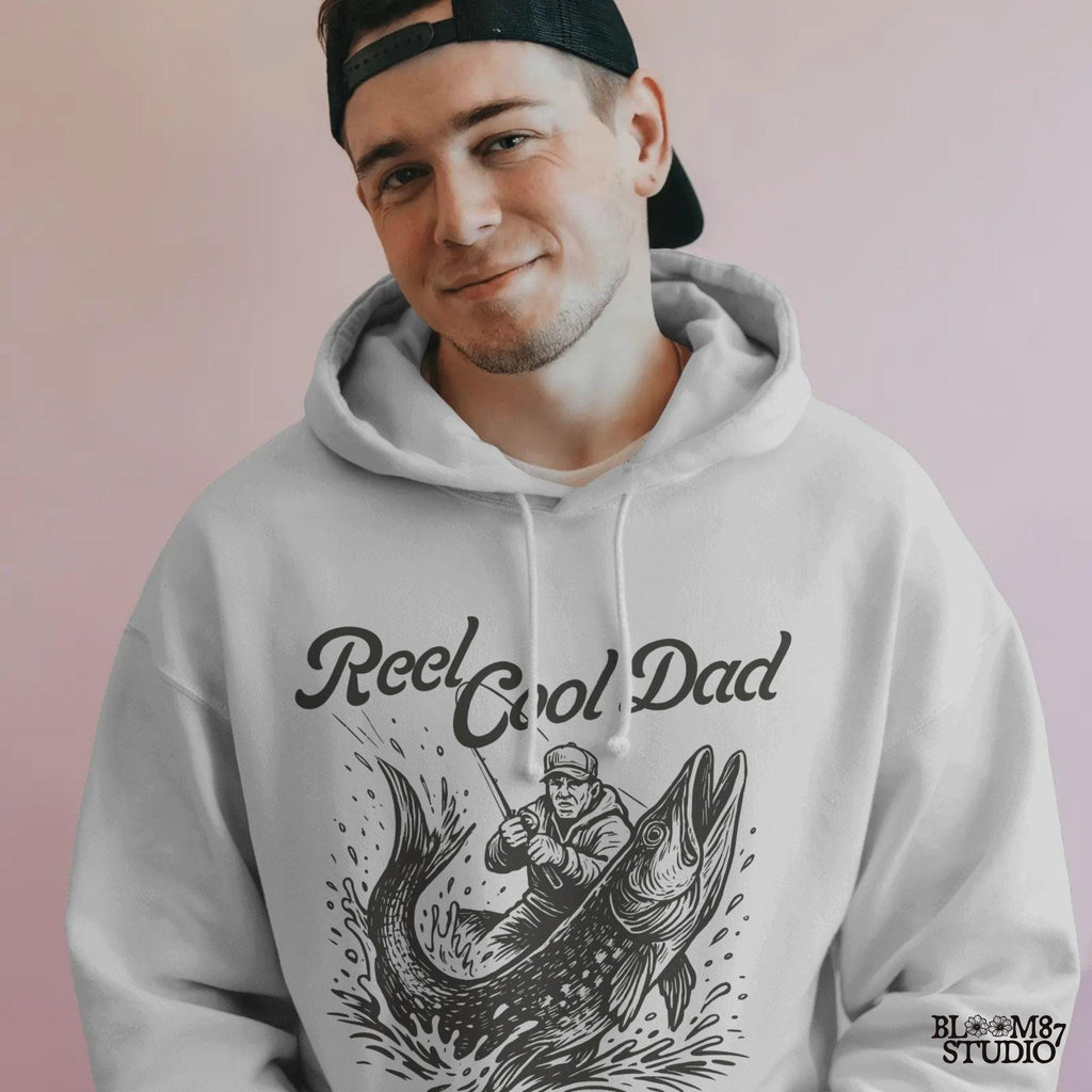 Illustration of a father reeling in a giant fish with bold text “Reel Cool Dad,” perfect for Father’s Day or fishing-themed gifts.