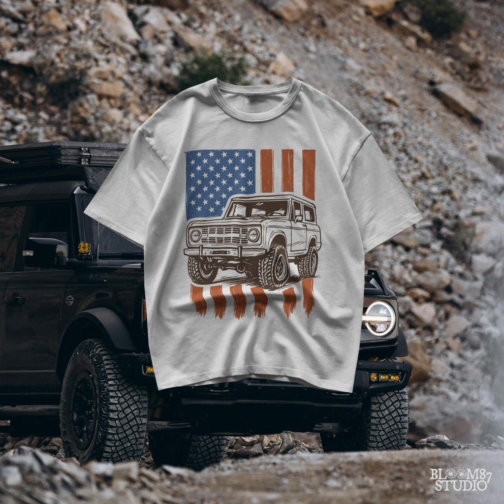 Vintage 4x4 Bronco-style off-road truck with bold tires over a distressed American flag, perfect for patriotic truck lovers and USA-themed designs.