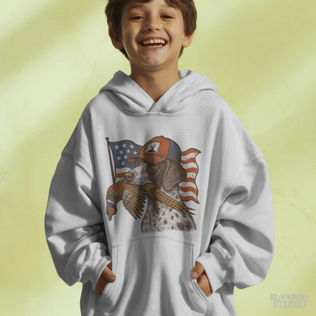 Hunting dog wearing a cap and holding a pheasant in its mouth, with a waving American flag in the background.