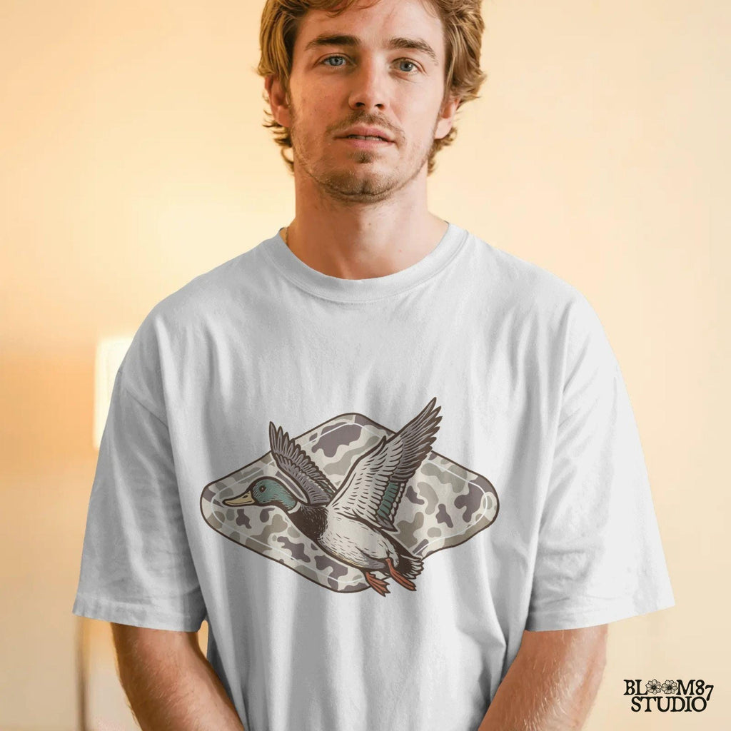 Flying mallard duck over old-school marsh camouflage background, designed in vintage hunting style for southern outdoorsman-themed crafts.