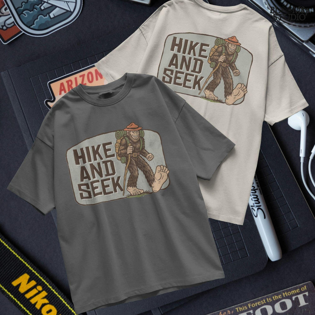 Illustration of a smiling Bigfoot wearing a ranger hat and hiking backpack with the phrase “Hike and Seek,” designed as a PNG for sublimation or print-on-demand products.