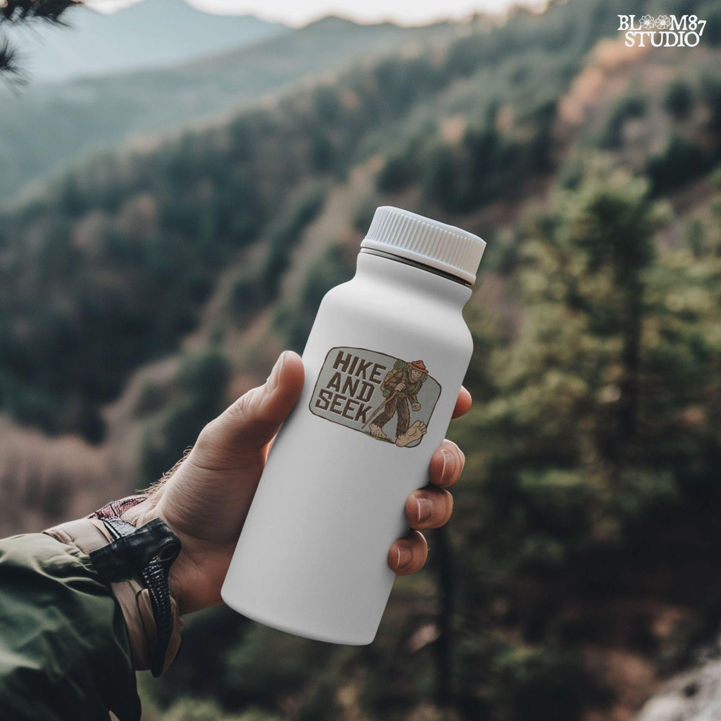 Illustration of a smiling Bigfoot wearing a ranger hat and hiking backpack with the phrase “Hike and Seek,” designed as a PNG for sublimation or print-on-demand products.