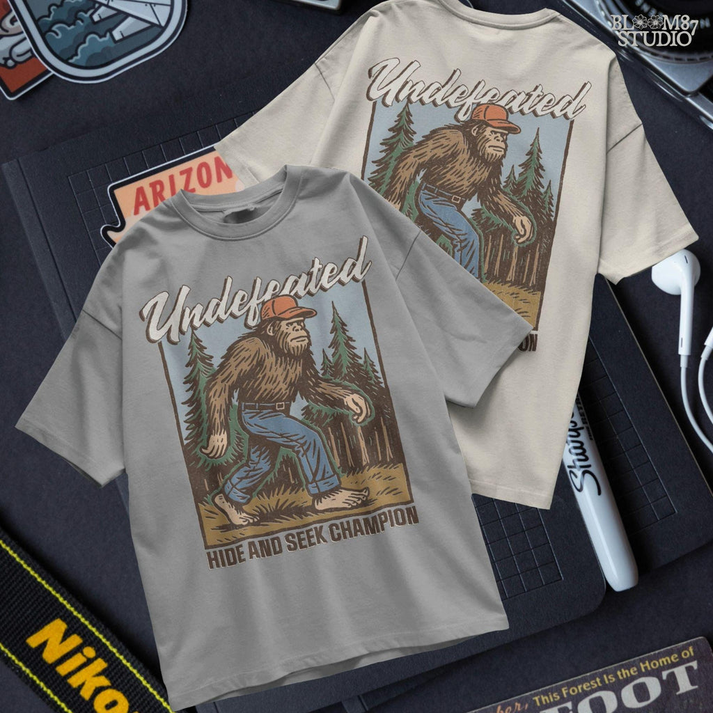 Hand-drawn Bigfoot walking through a pine forest in a red cap and jeans, with text “Undefeated Hide and Seek Champion,” designed for sublimation use.