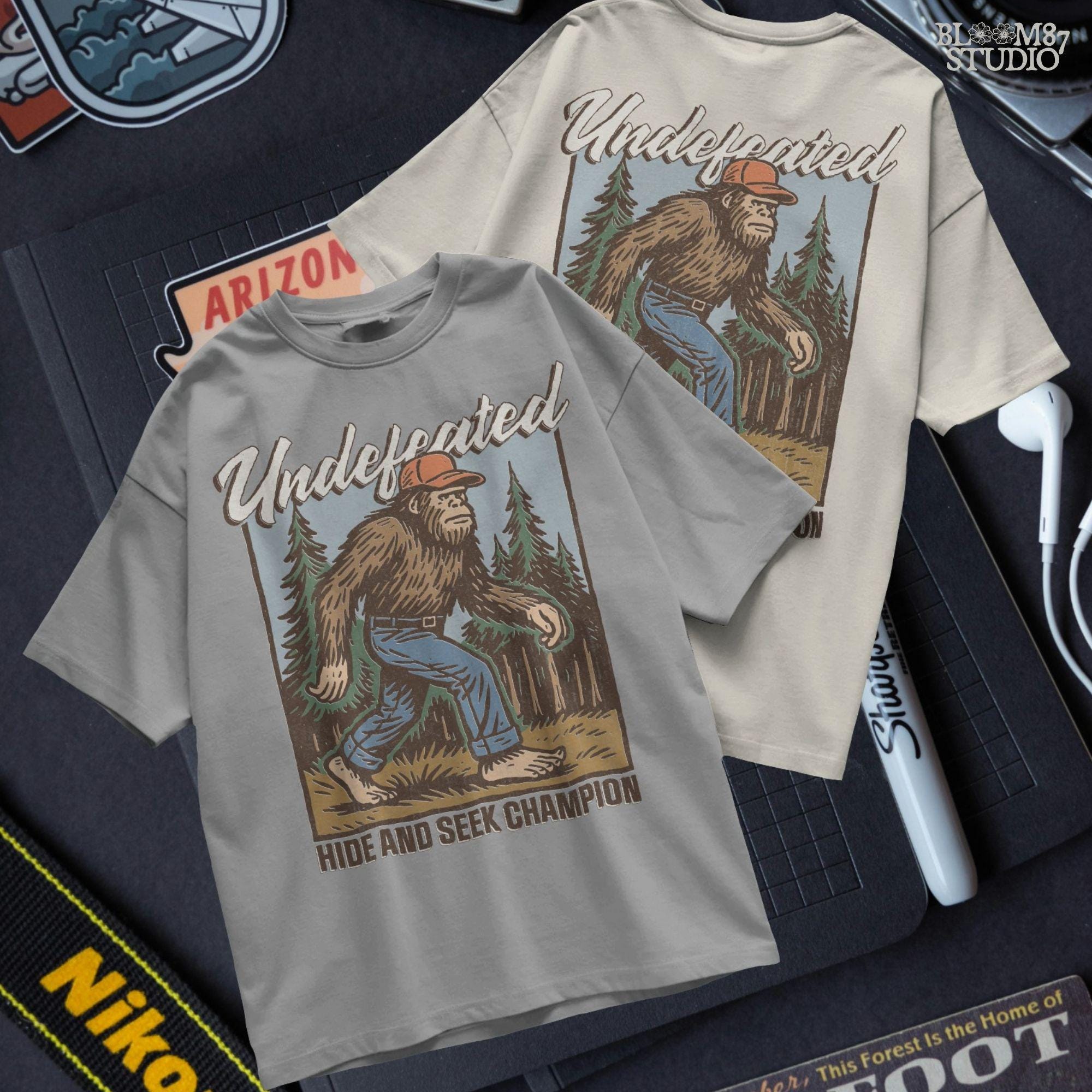 Hand-drawn Bigfoot walking through a pine forest in a red cap and jeans, with text “Undefeated Hide and Seek Champion,” designed for sublimation use.