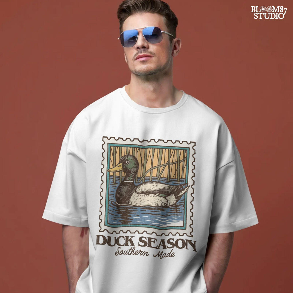 Vintage stamp-style mallard duck floating in water with forest background and text “Duck Season – Southern Made” in retro serif font.