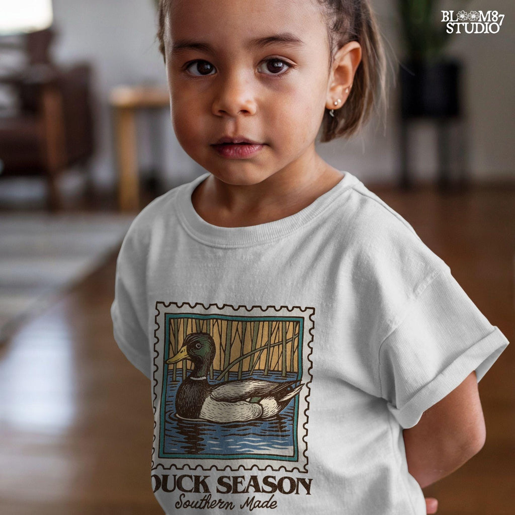 Vintage stamp-style mallard duck floating in water with forest background and text “Duck Season – Southern Made” in retro serif font.