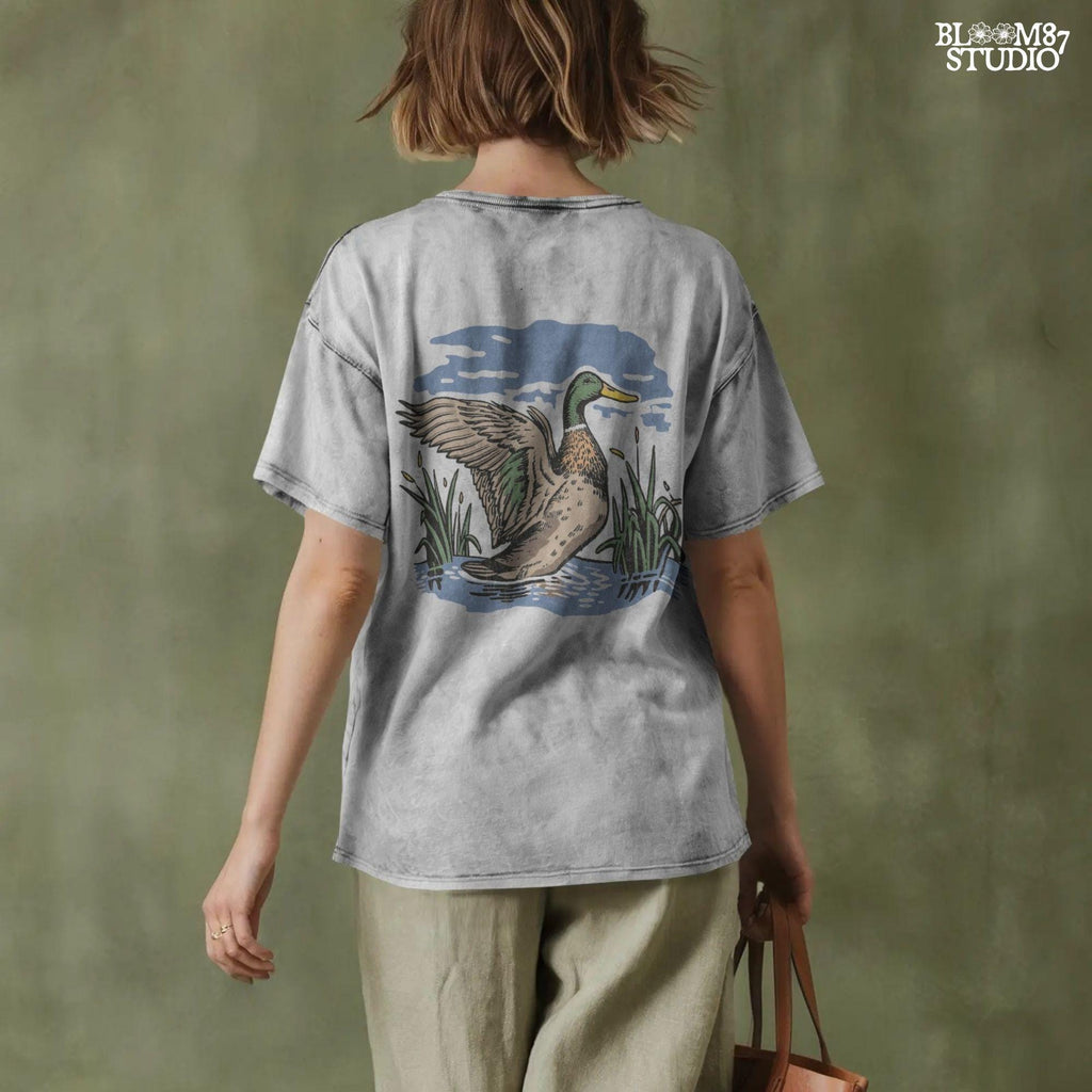 Vintage illustration of a mallard duck with wings spread standing in a pond with reeds and a cloudy blue sky – rustic nature sublimation PNG.