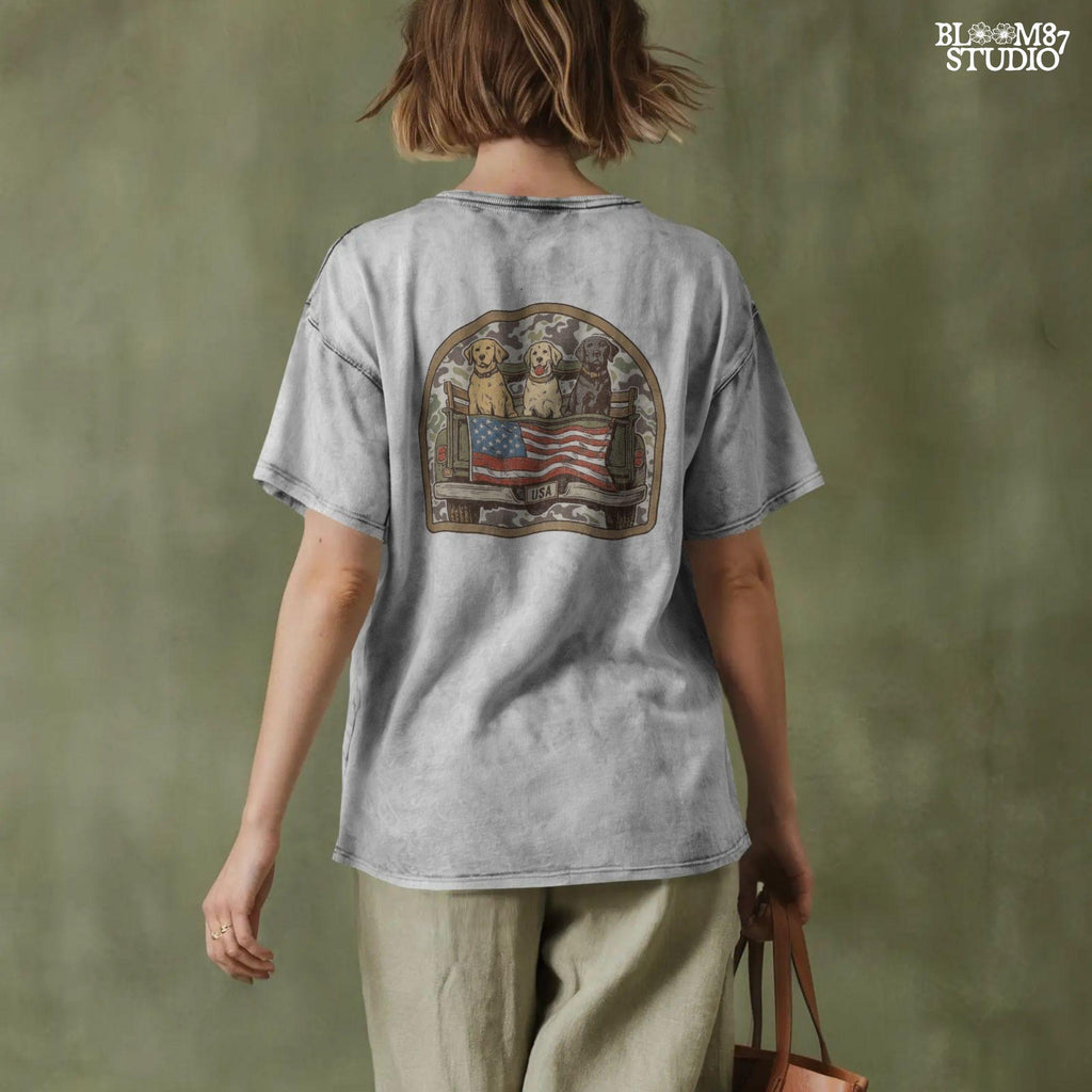 Three Labrador retrievers — yellow, chocolate, and black — sitting on the back of a green camouflage pickup truck with an American flag and the words “Local Boy” underneath.