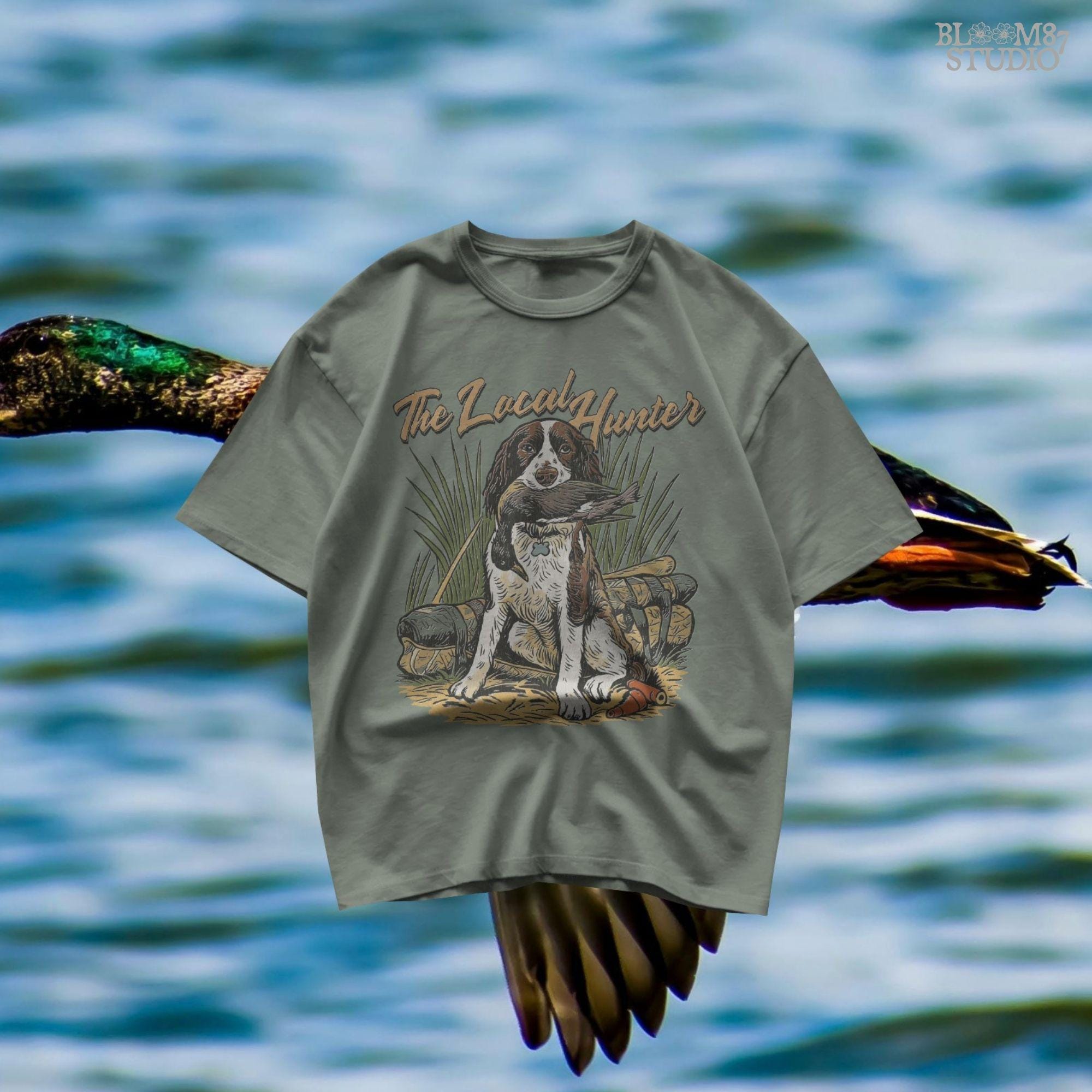 Vintage illustration of a Springer Spaniel hunting dog holding a duck in its mouth with grass, ammo, and hunting gear around, and the phrase “The Local Hunter” above.