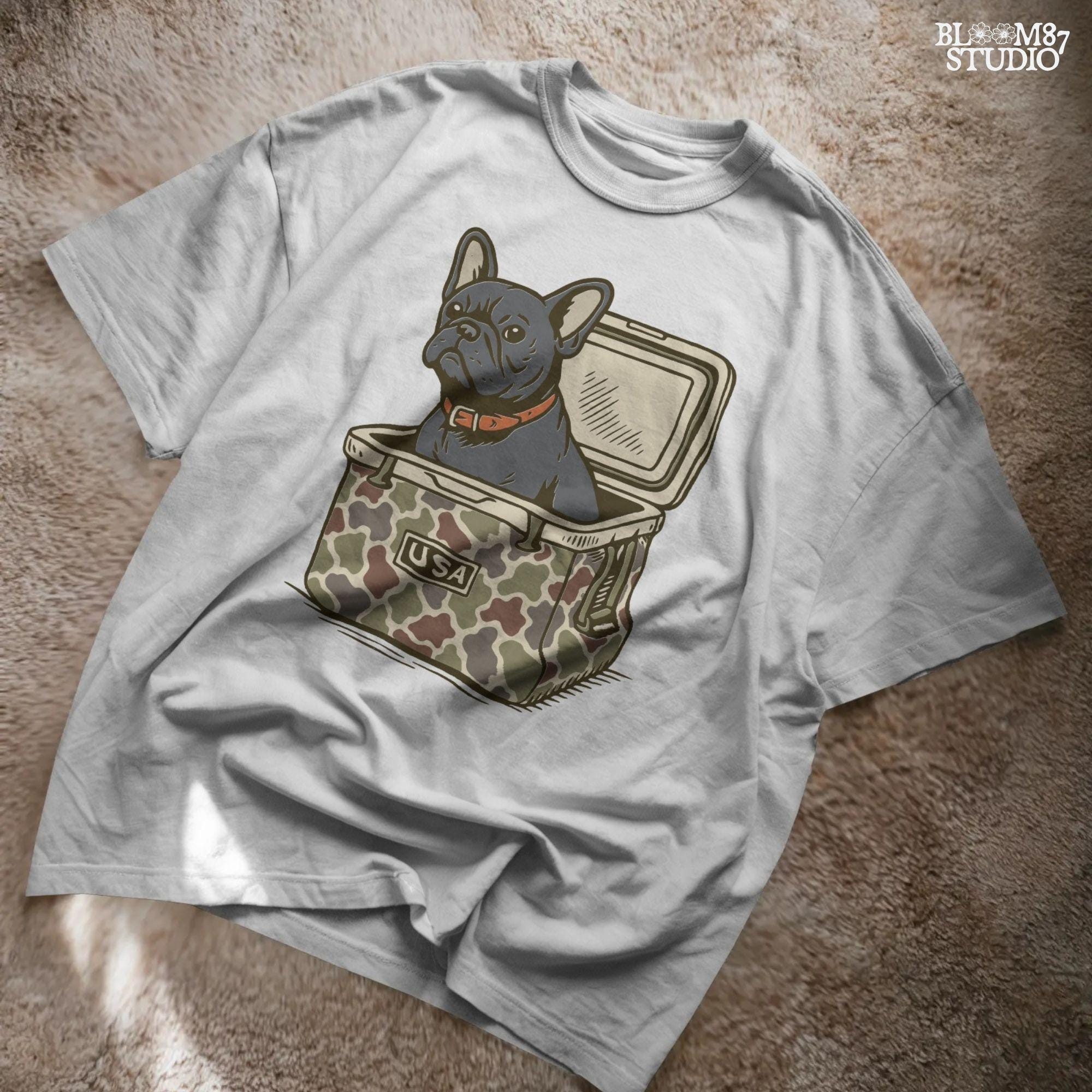 French Bulldog sitting inside a camouflage USA cooler, wearing a red collar, in rustic outdoor style — perfect for patriotic dog lovers and sublimation use.