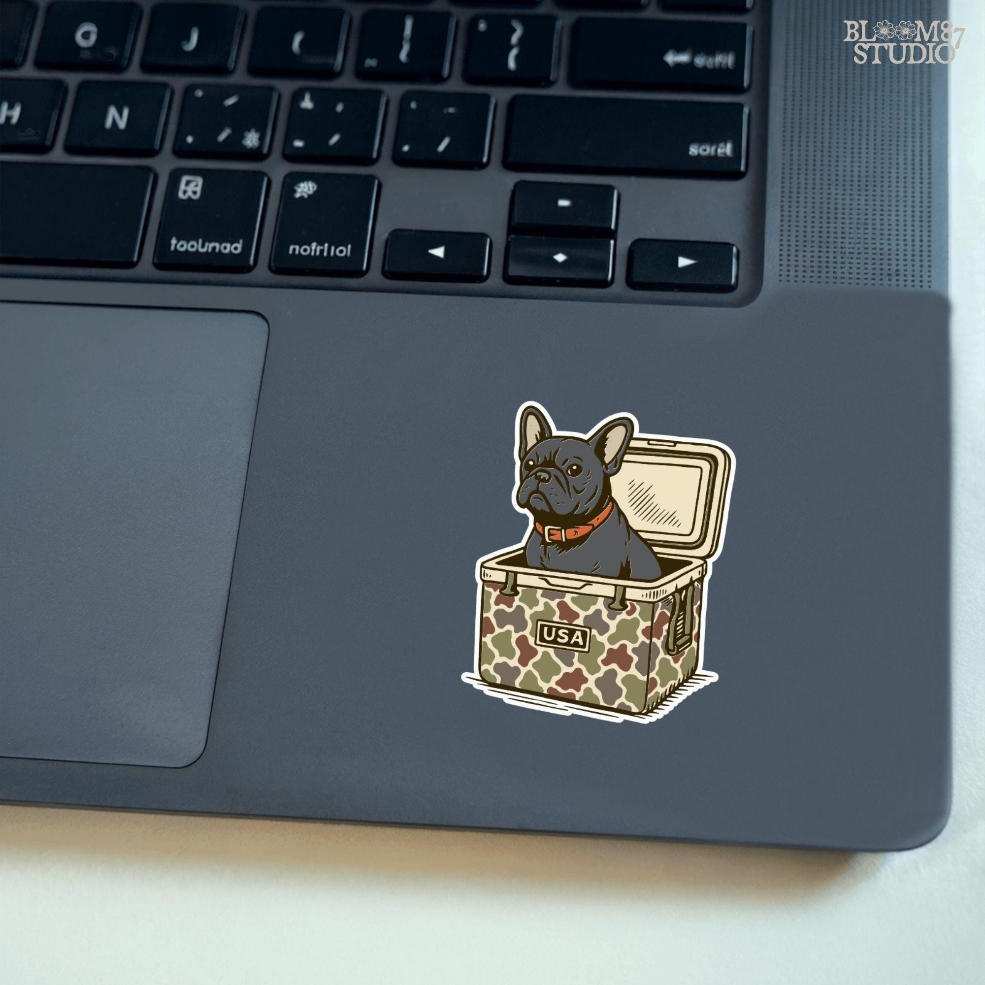 French Bulldog sitting inside a camouflage USA cooler, wearing a red collar, in rustic outdoor style — perfect for patriotic dog lovers and sublimation use.