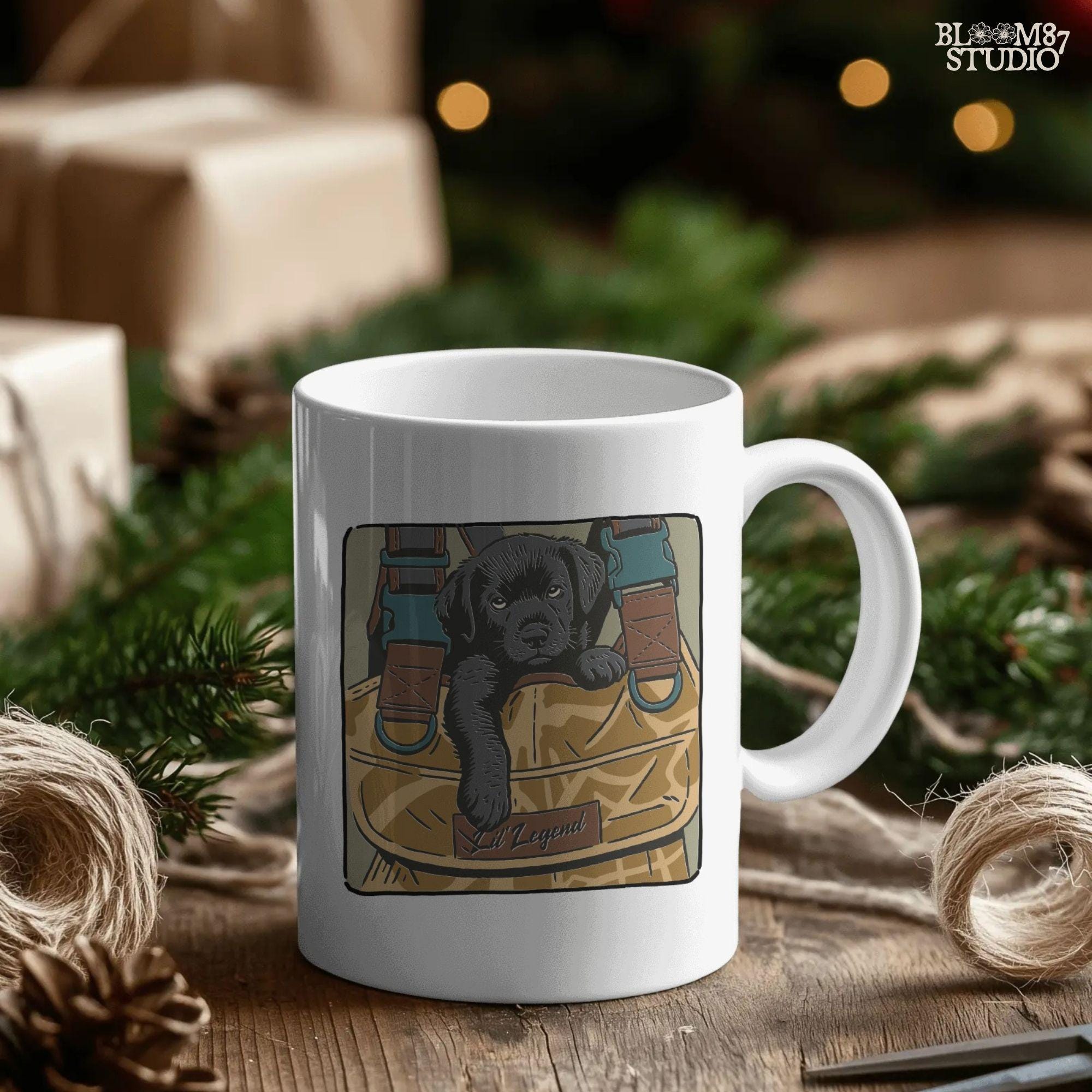 Illustration of a black Labrador puppy resting in a camouflage hunting bag with a “Lil’ Legend” tag – ideal for outdoor-themed sublimation projects.